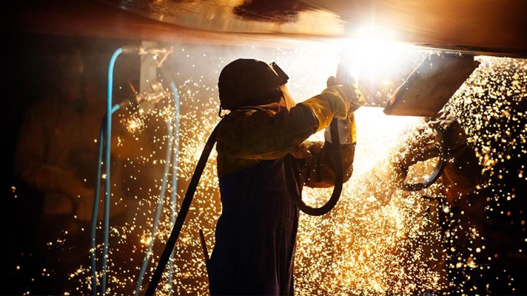 Person welding wearing coveralls and helmet sparks cascading