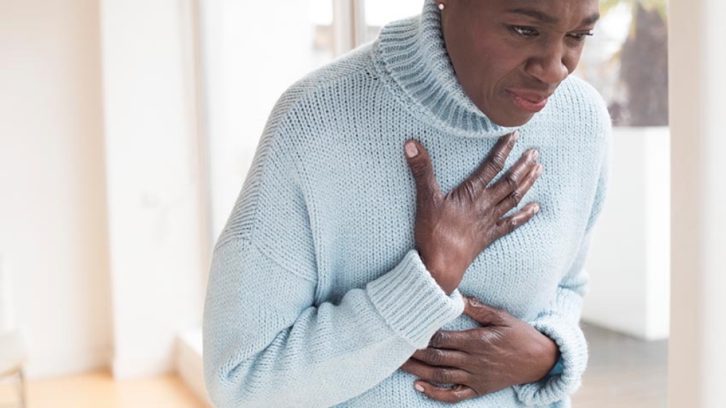 Woman bent over holding chest in light blue sweater.