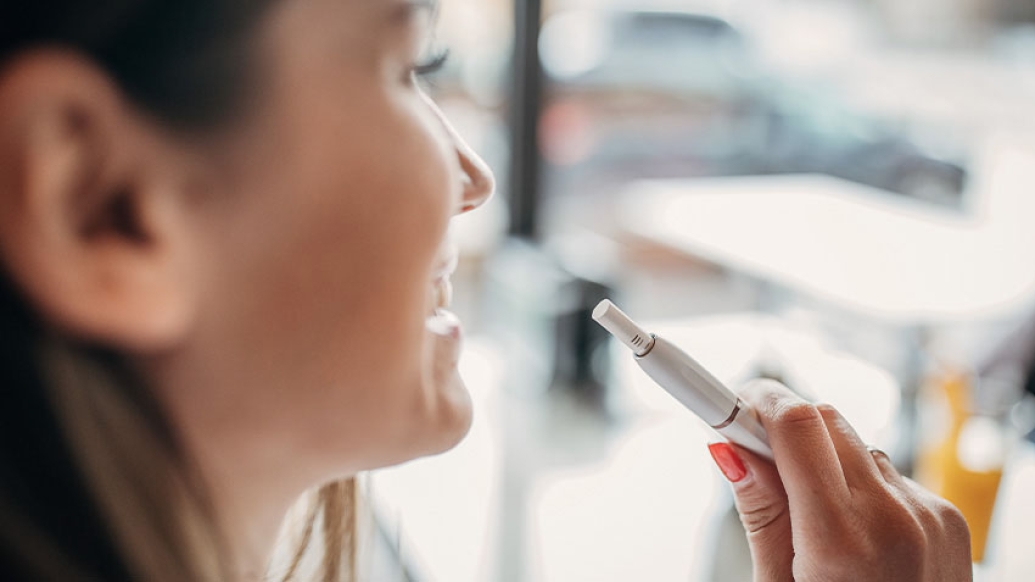 Woman looking out window smoking electric cigarette