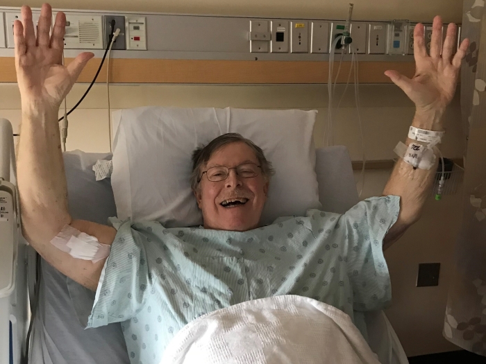 older man holding hands up over head celebrating in hospital bed 