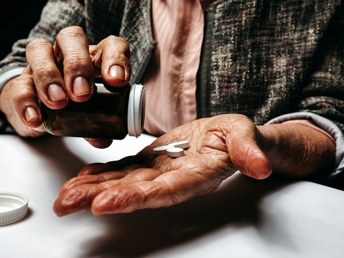older person pouring pills into hand close up