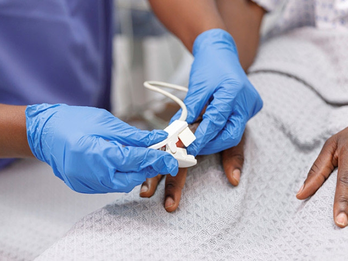 Patient in hospital bed having oxygen reading by provider with blue gloves on