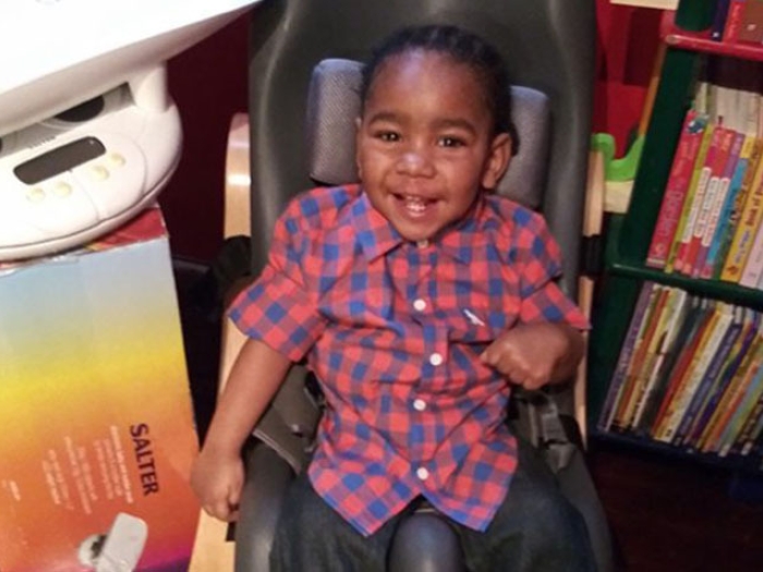 child sitting in red shirt checkered smiling