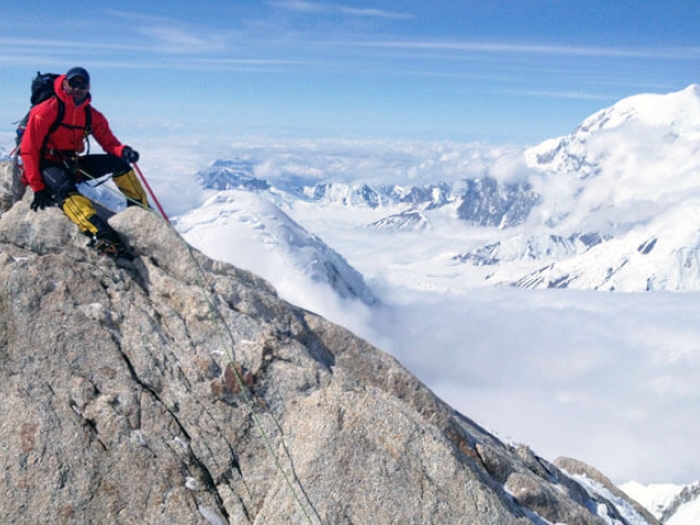 Climber in red coal sitting on mountain summit