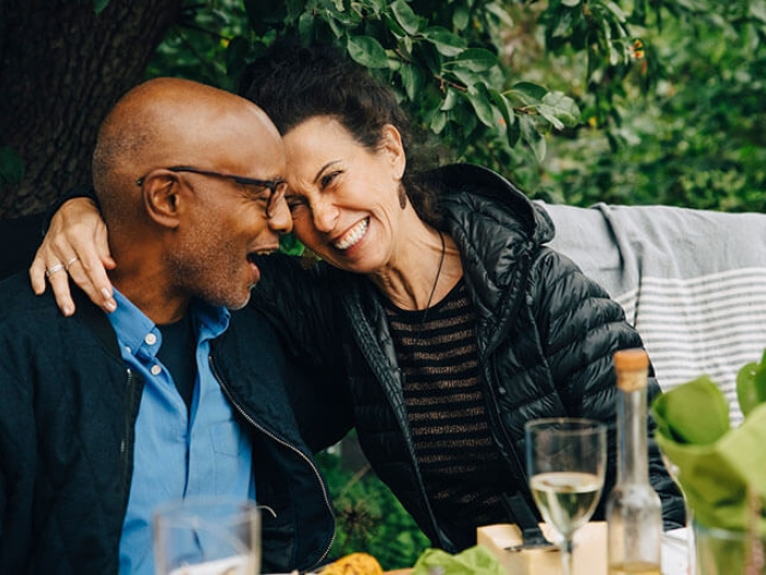 Couple sitting at table with wine, garden in background, woman with arm around man.