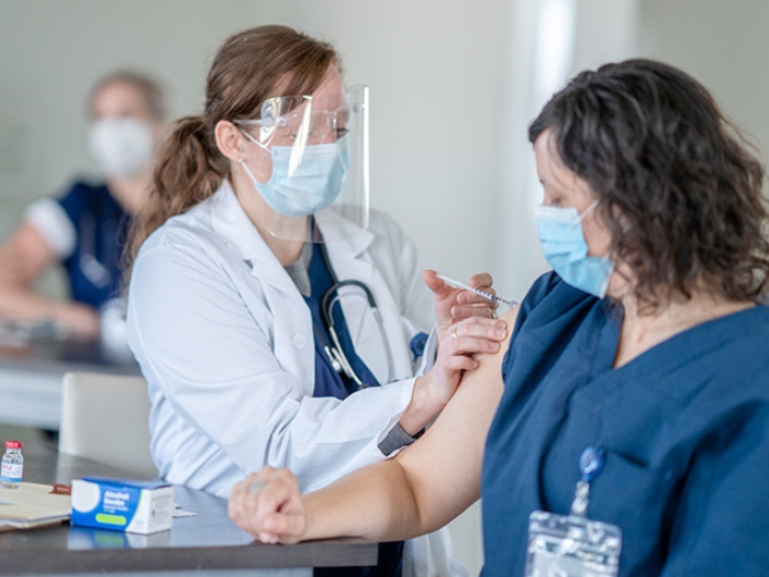 health care worker with face shield giving shot to woman with both wearing masks