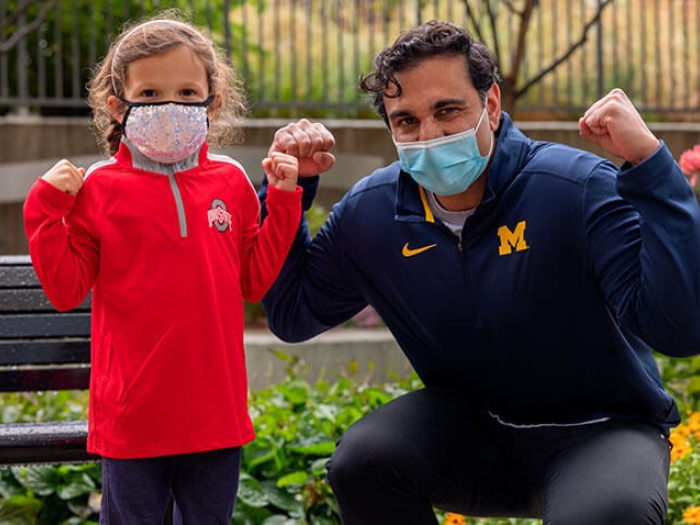 Chloe and doctor making strong arms, pink jacket and doctor in Michigan jacket with masks.