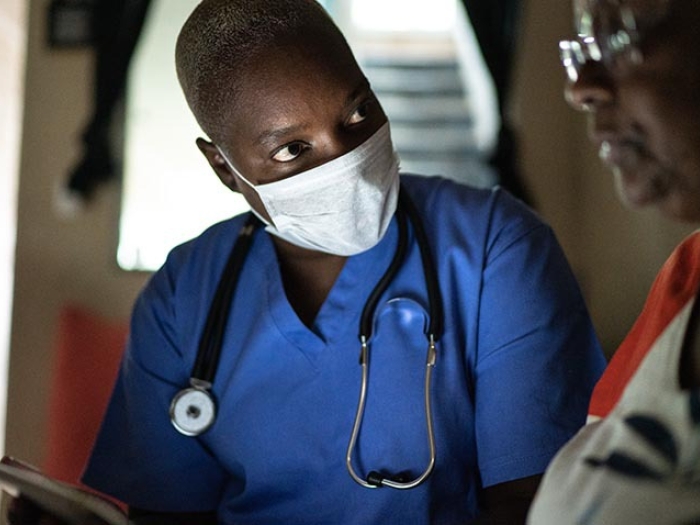 health visitor in blue scrubs and stethoscope and woman during home visit using digital tablet