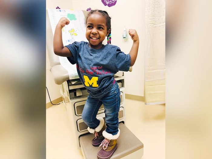 little girl doing muscle pose in doctor's office wearing a blue Michigan shirt