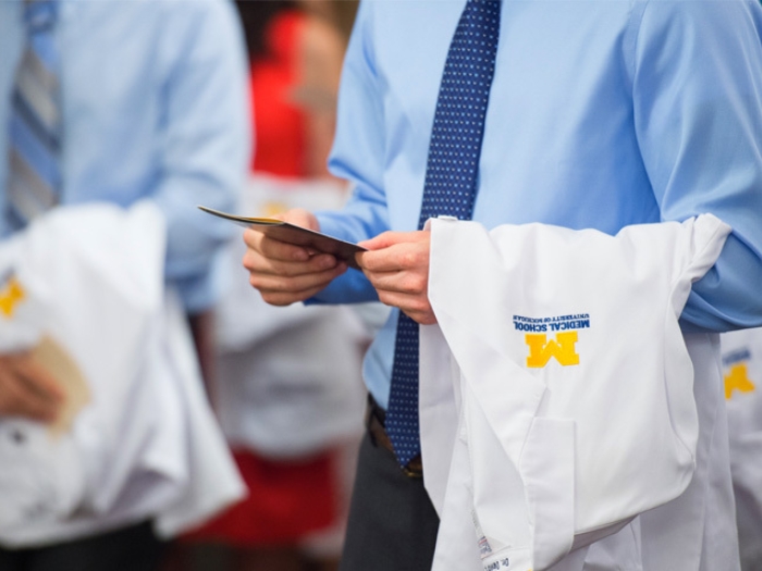 man holding white coat in hand with business shirt and tie on in blue