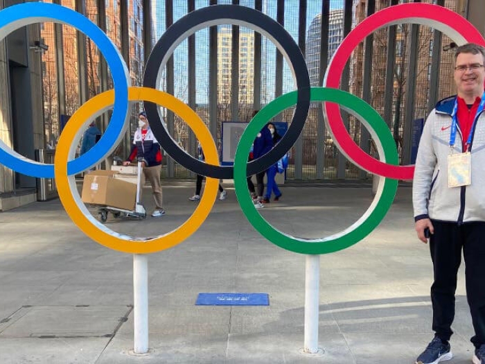 Man in white jacket standing near Olympic rings