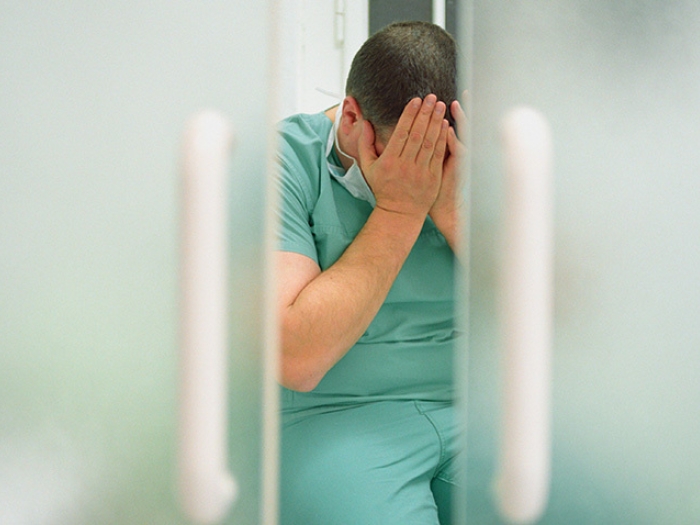 man scrubs holding hands over face sad through door