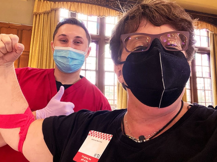 masked woman with glasses smilling with red gauze on arm and nurse standing behind masked giving thumbs up