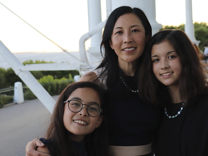 two daughters and mother smiling at camera outside on white bridge wearing black