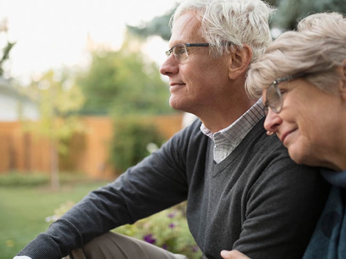 Older woman leaning on shoulder of older man sitting outside.