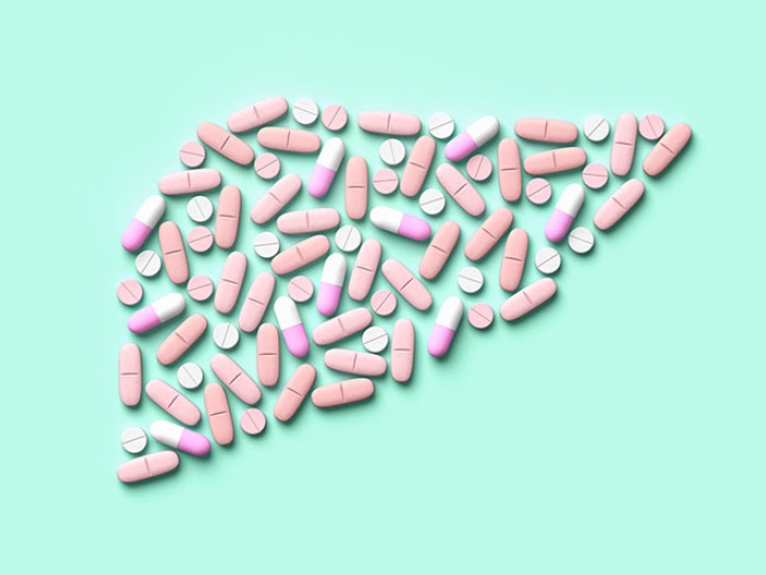 Pills medicine shaped of liver organ on teal background