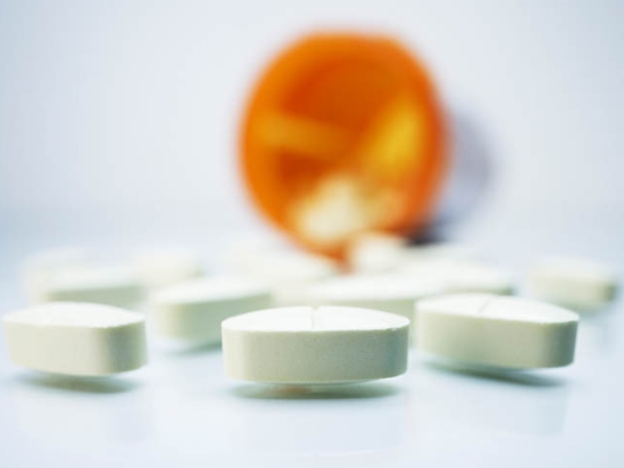 Pills spilled out of orange bottle on white surface.