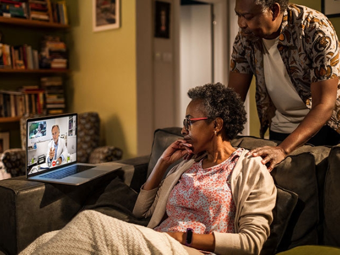 senior couple on couch with doctor on laptop