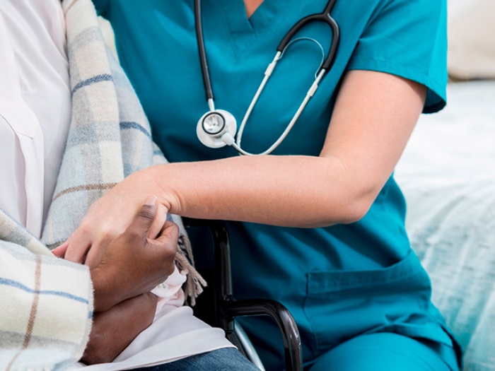 senior patient holding arm and hands with nurse with blue scrubs on
