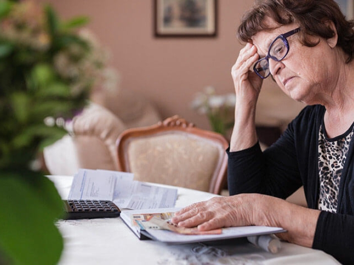 Senior woman with hand on head looking at book with calculator next to her at table