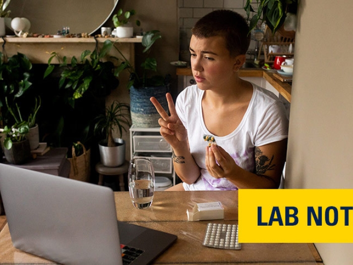 teen sitting on laptop with pills in hand in kitchen