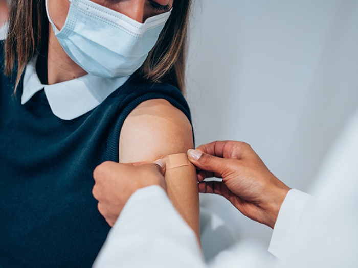 girl with navy shirt and white collar getting band aid put in arm with mask on