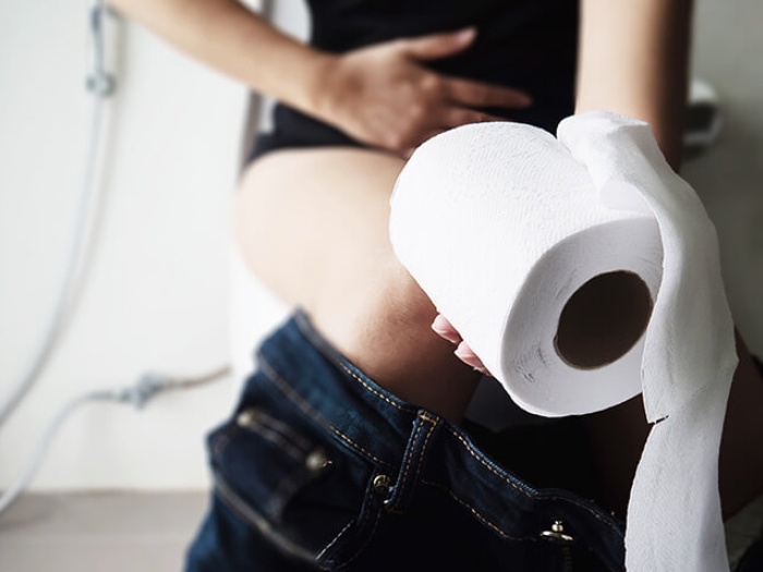 Women sitting on toilet holding stomach and a roll of toilet paper