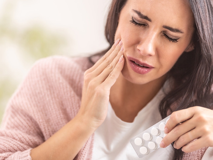 woman tooth pain holding pills in pink shirt