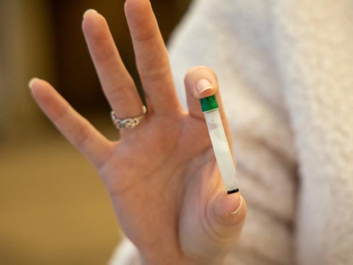 woman holding clear vial with green lid in two fingers