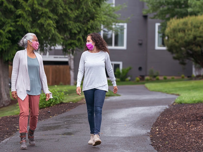 women walking outside on black path with masks on talking