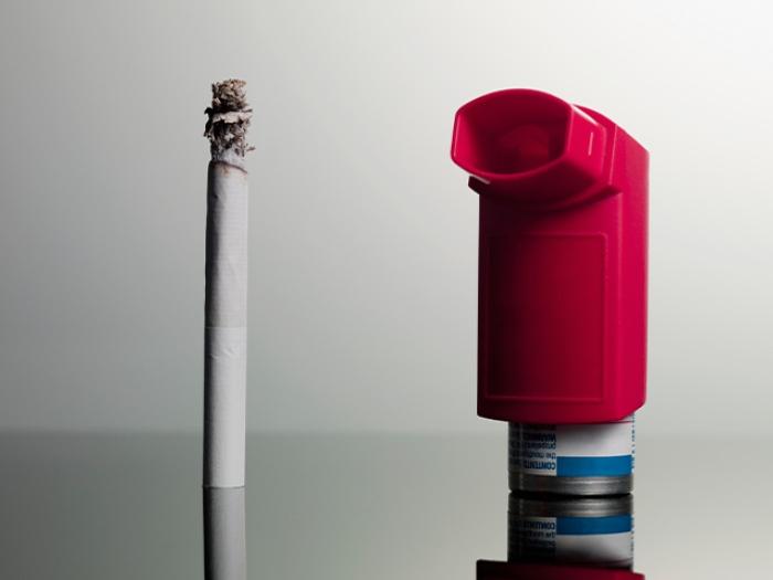burning white cigarette and red inhaler grey background