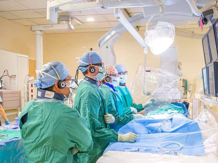 Doctors and nurses in surgery room performing surgery and looking at monitors.