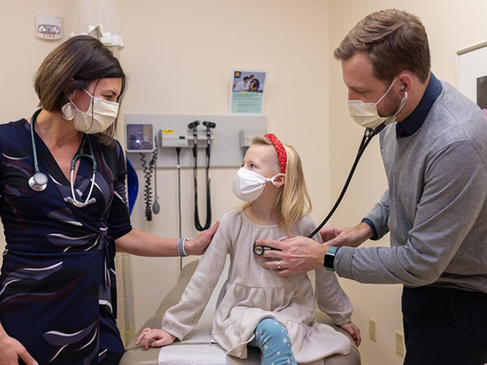 doctors with blonde child in exam room checking heart