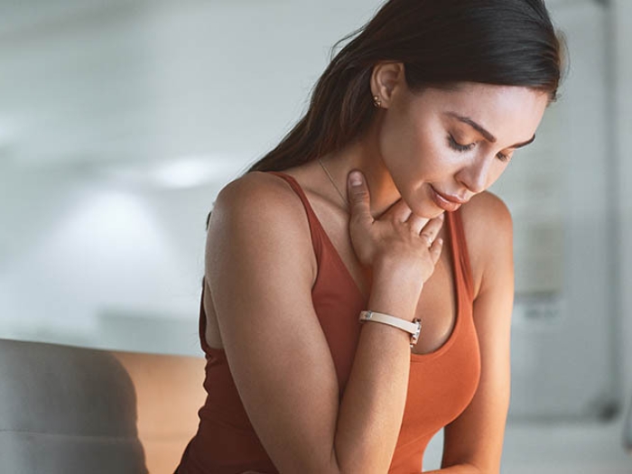 female wearing orange tank top holding her throat in discomfort and looking down