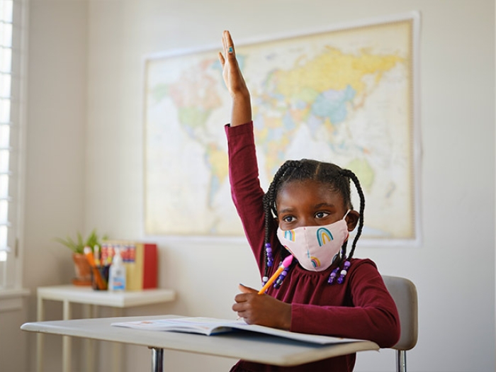 kid at school wearing mask raising hand