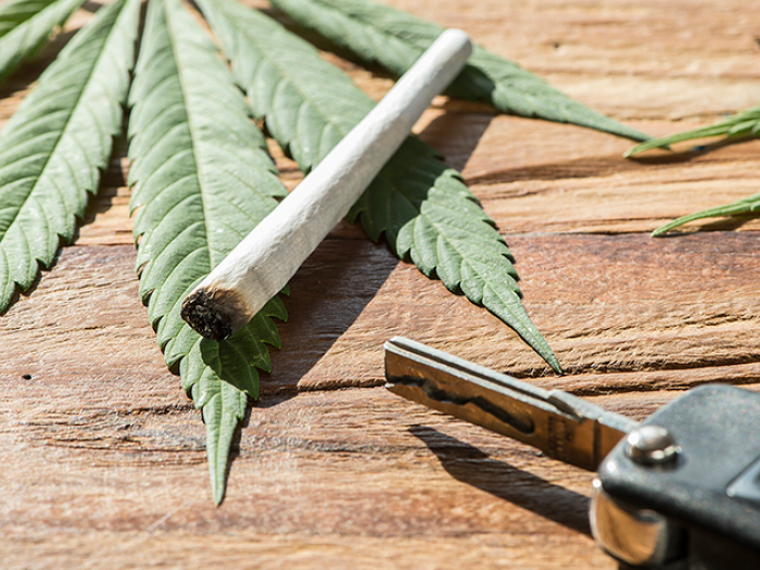 Car key and a marijuana cigarette laying on cannabis leaves