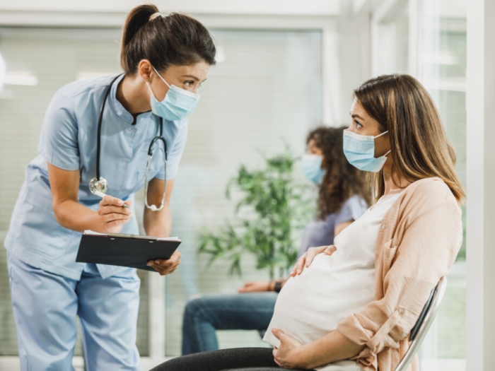 health care worker leaning over to talk to pregnant women in mask sitting