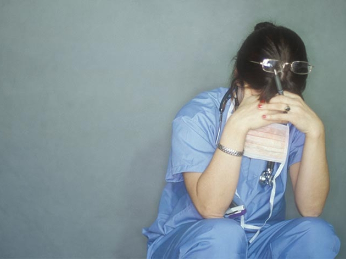 health care worker crouched down with hands on forehead stressed