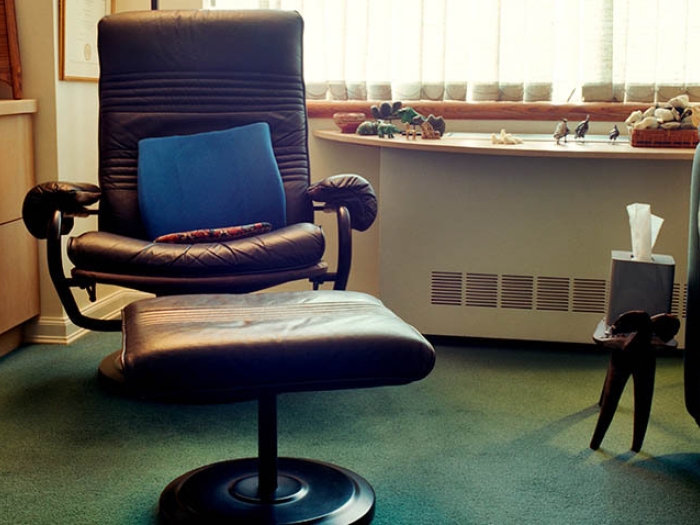 maroon office chair with blue pillow in it with foot rest and green couch next to it with green carpet on floor