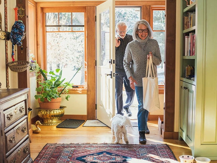 Older couple entering into home with bags of groceries.