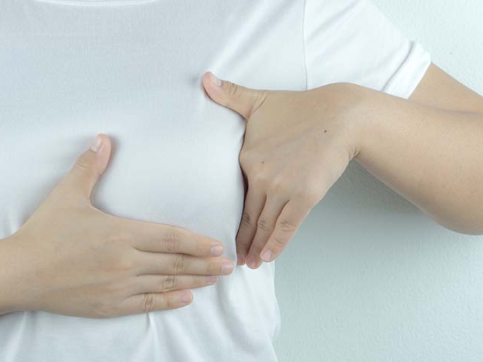 person doing self breast exam over white shirt