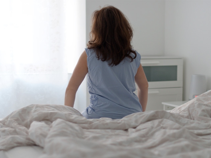 woman sitting on bed blue shirt white sheets wall