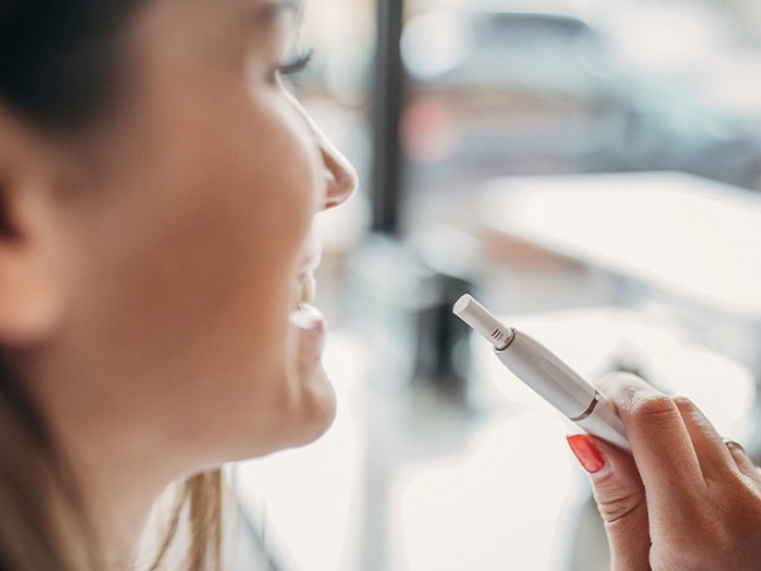 Woman looking out window smoking electric cigarette