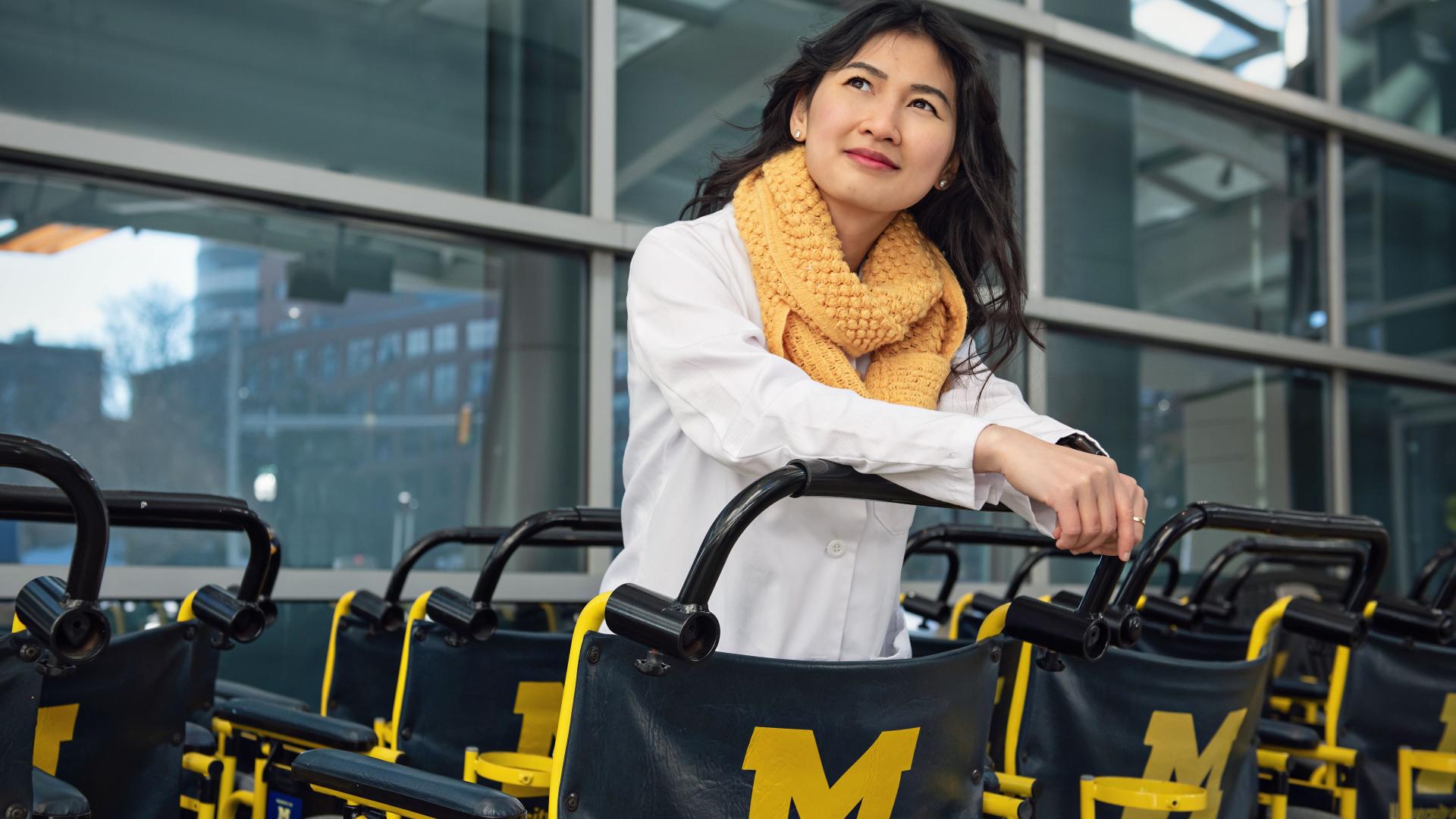 women in labcoat and scarf standing among a fleet of Michigan Medicine wheelchairs